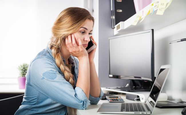 Zestresowana kobieta przed komputerem rozmawia przez telefon