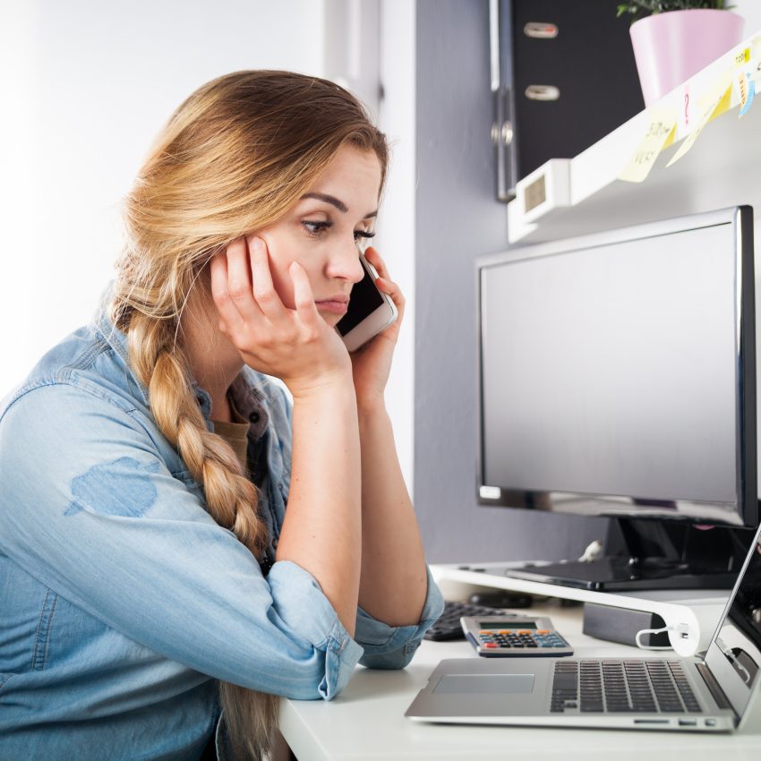 Zestresowana kobieta przed komputerem rozmawia przez telefon