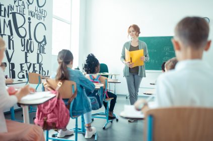 Nauczycielka stoi naprzeciw uczniów w klasie