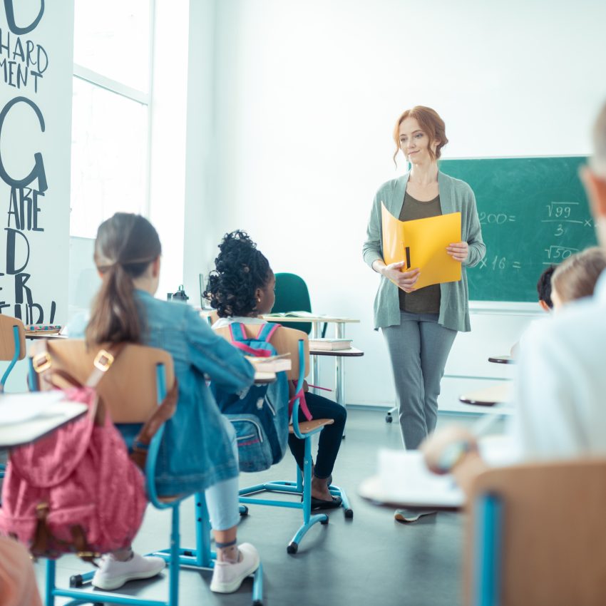 Nauczycielka stoi naprzeciw uczniów w klasie