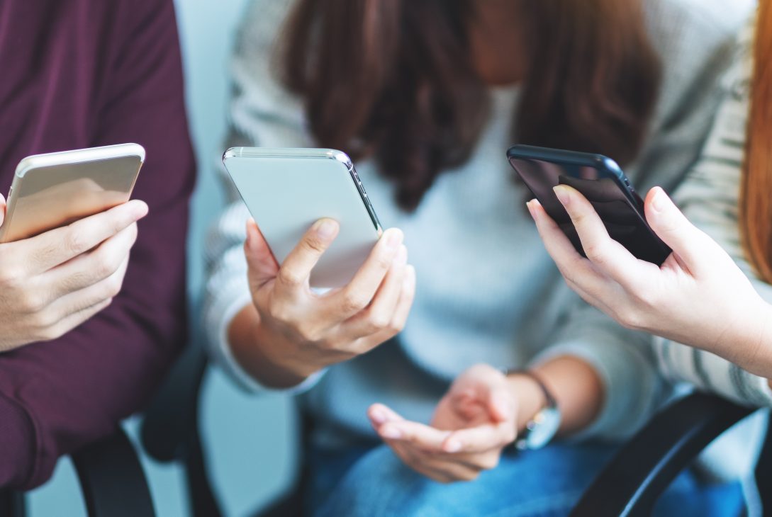 Grupa młodych ludzi przegląda swoje smartfony siedząc razem