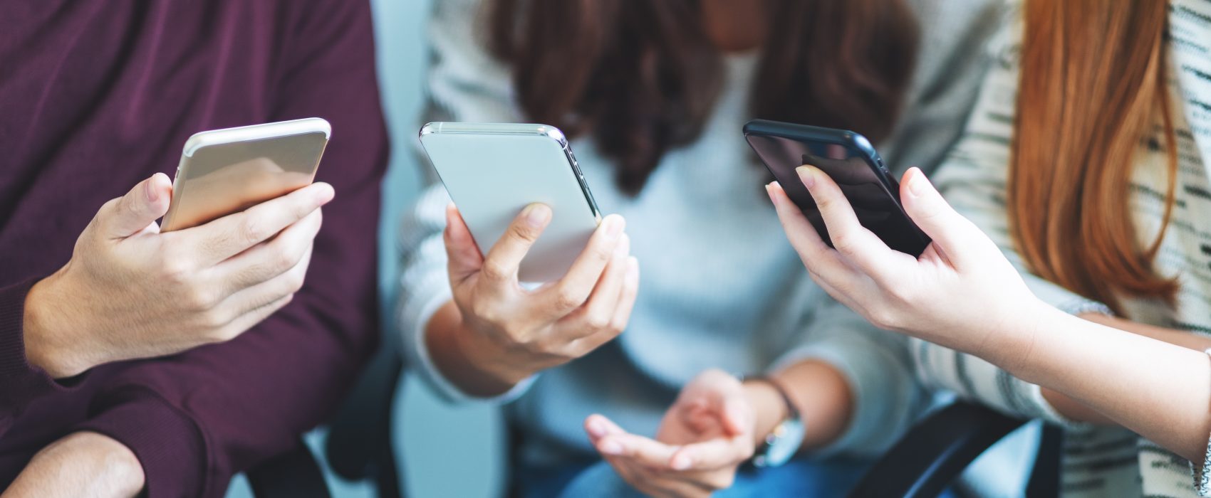 Grupa młodych ludzi przegląda swoje smartfony siedząc razem