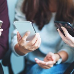 Grupa młodych ludzi przegląda swoje smartfony siedząc razem
