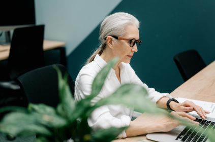 Starsza pani wpisuje tekst na klawiaturze laptopa