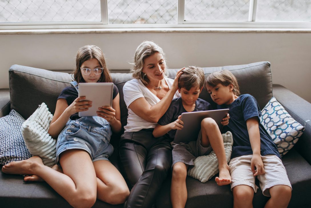 Mama i dzieci z tabletami siedzą na sofie.