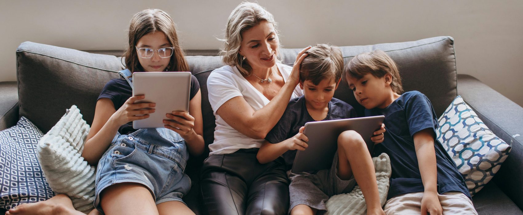 Mama i dzieci z tabletami siedzą na sofie.