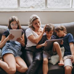 Mama i dzieci z tabletami siedzą na sofie.