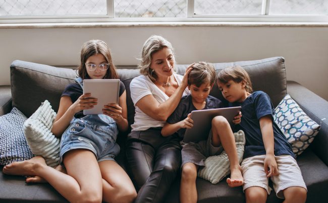 Mama i dzieci z tabletami siedzą na sofie.