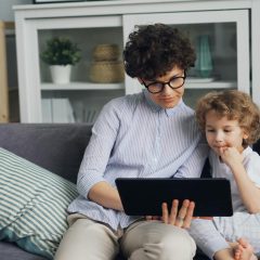 Dzieci siedzą na sofie i oglądają coś na tablecie
