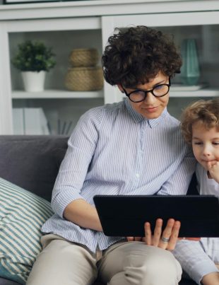 Dzieci siedzą na sofie i oglądają coś na tablecie