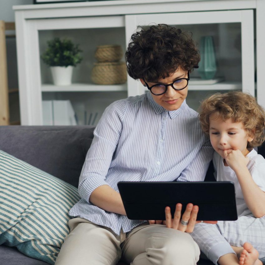 Dzieci siedzą na sofie i oglądają coś na tablecie